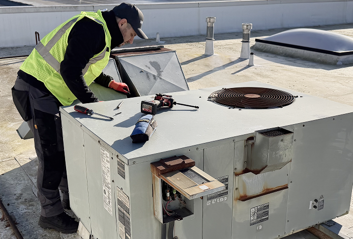 Licensed technician performing routine commercial HVAC maintenance on a rooftop unit